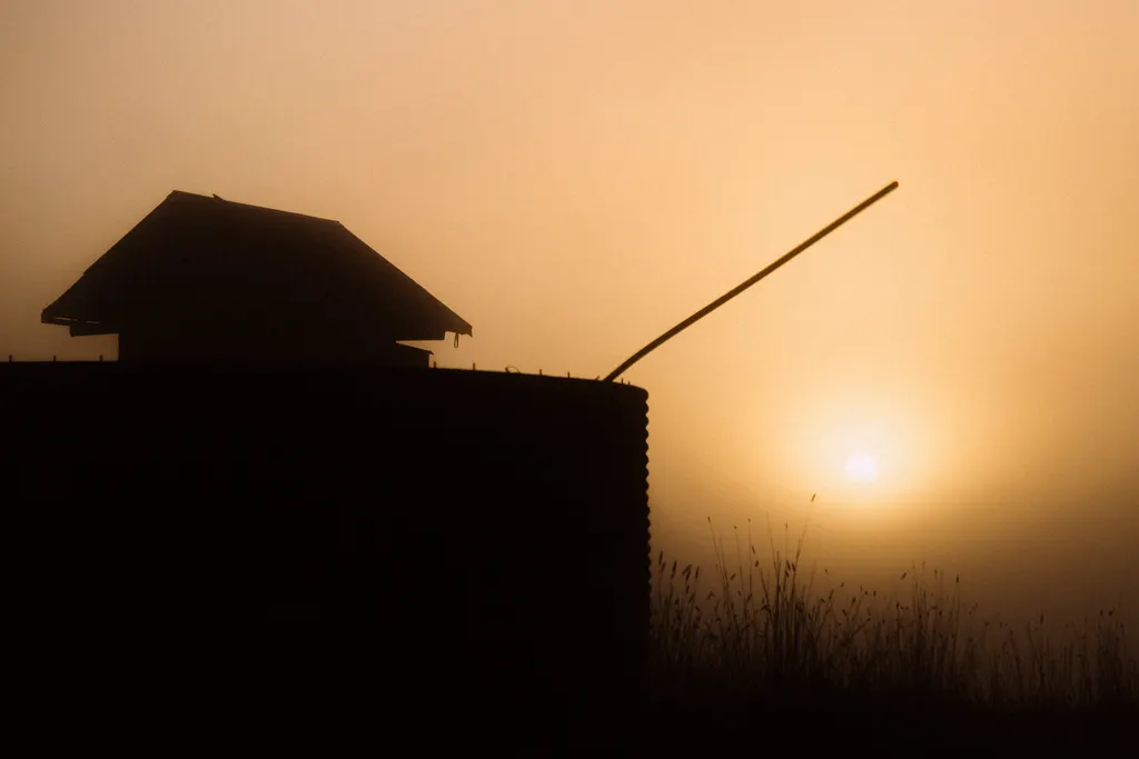 Silhouette of a historic fort structure with a long wooden pole against a golden sunset sky.
