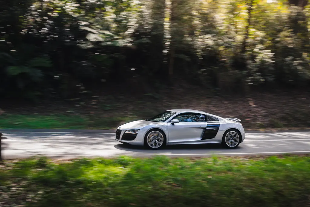 Silver sports car driving on a tree-lined road with motion blur in the background.