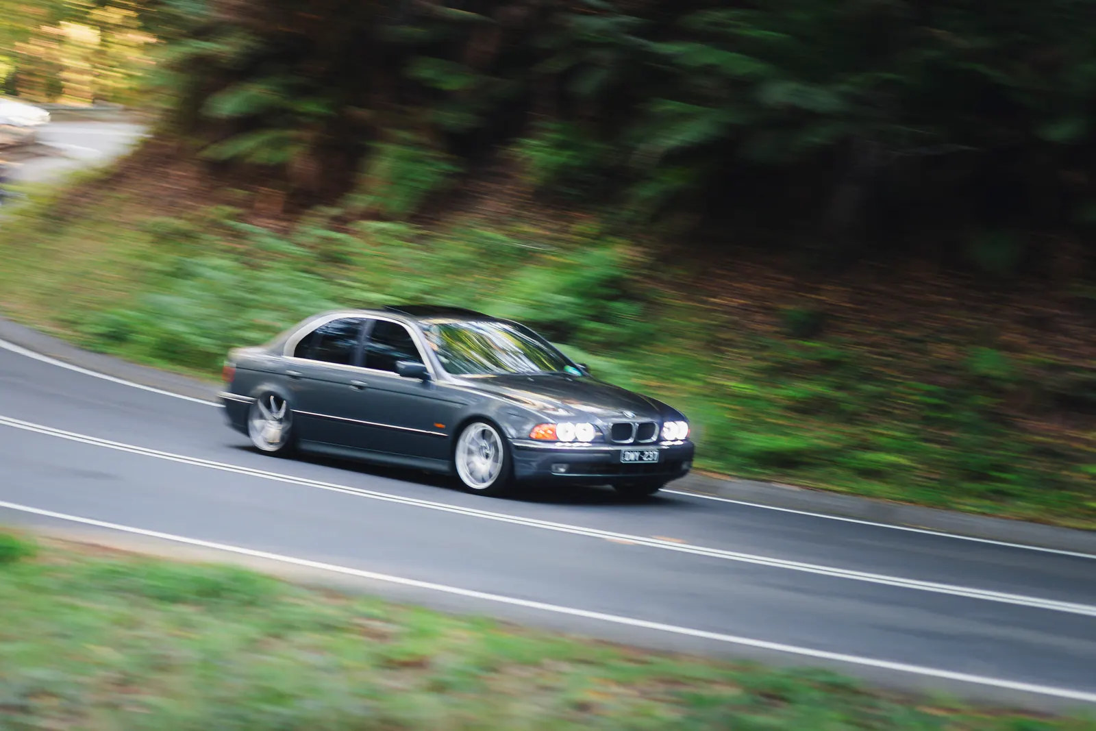 Dark sedan driving on a curved road surrounded by green forest and trees.