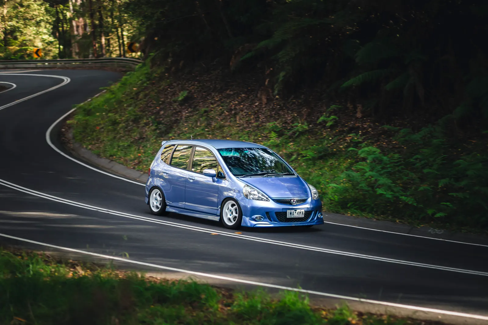 Blue hatchback navigating a winding forest road with white line markings.