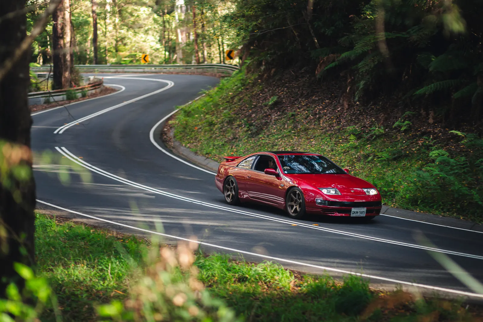 Red sports car navigating a winding forest road with white center line markings.