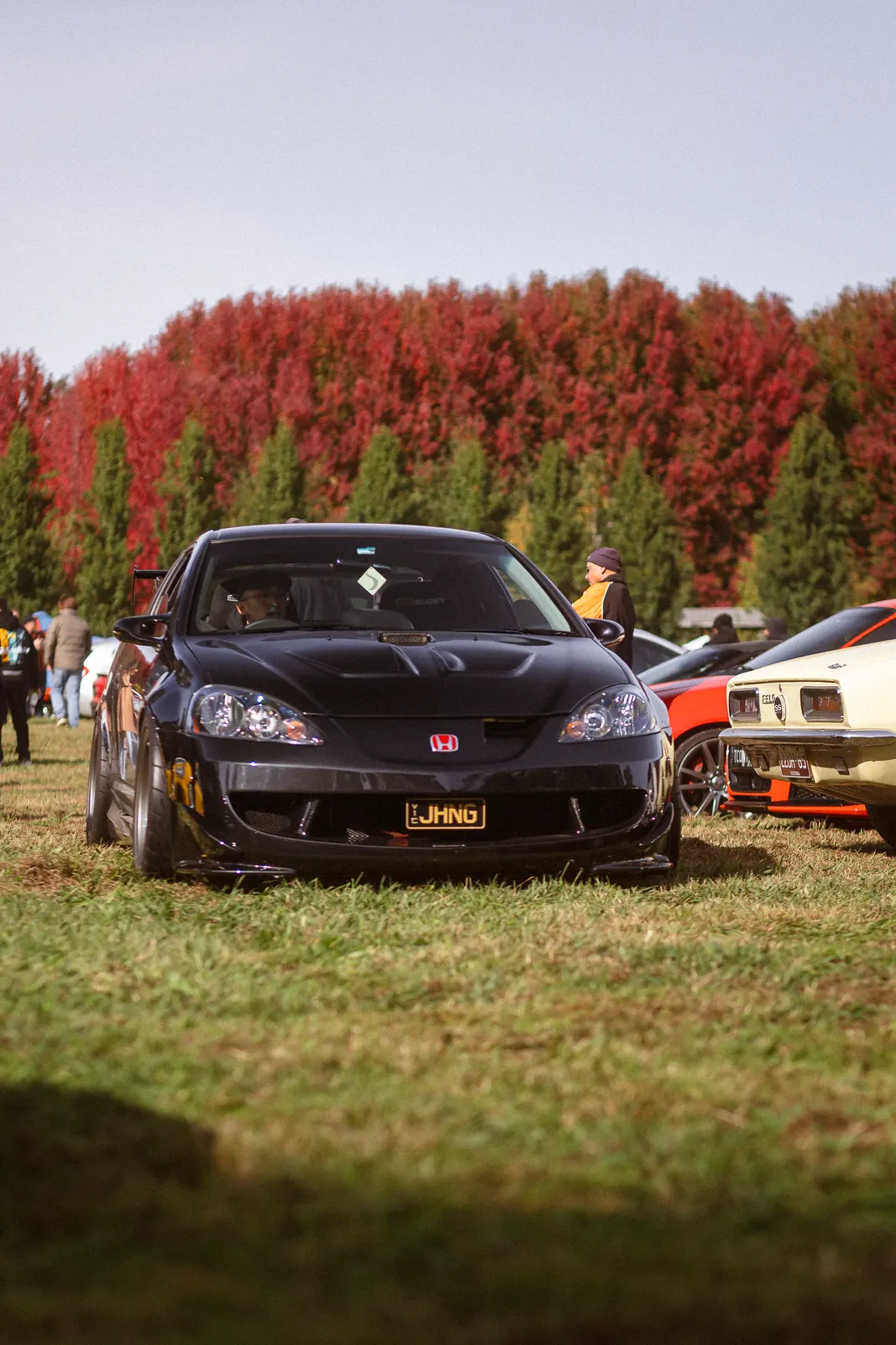 Black Honda sports car displayed at an outdoor car meet with autumn-colored trees in the background.