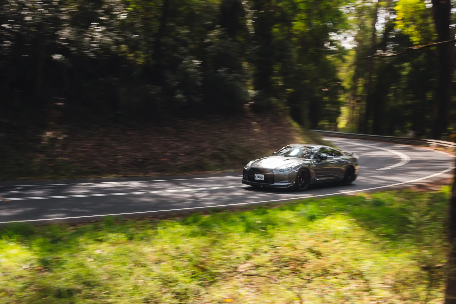 A silver sports car navigates a curved mountain road bordered by dense green forest.