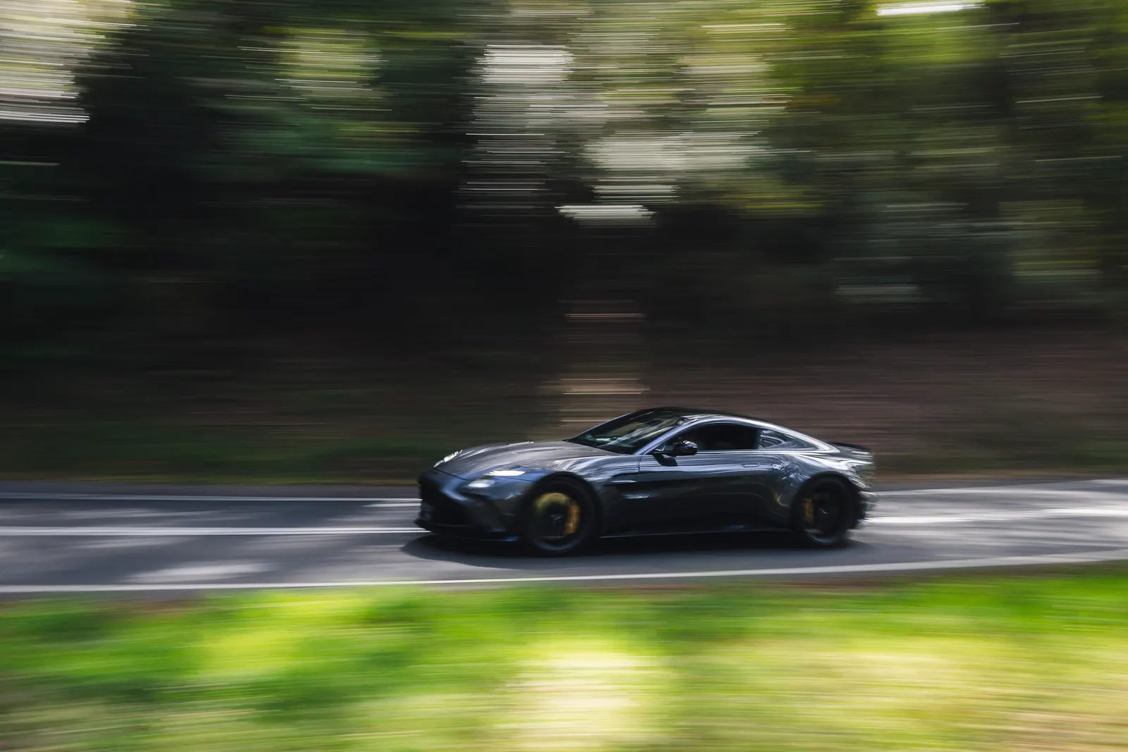 Dark blue sports car driving on a tree-lined road with motion blur effect